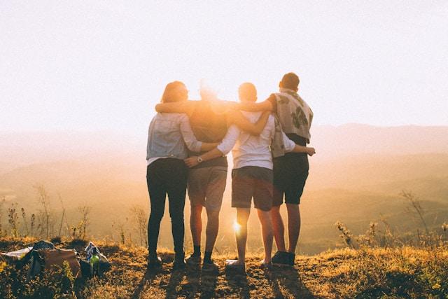 Quatre personnes de dos enlacés devant des collines avec le soleil