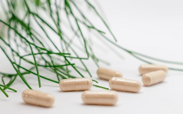 Gélules de complément alimentaire beiges avec des feuilles vertes en arrière-plan sur fond blanc