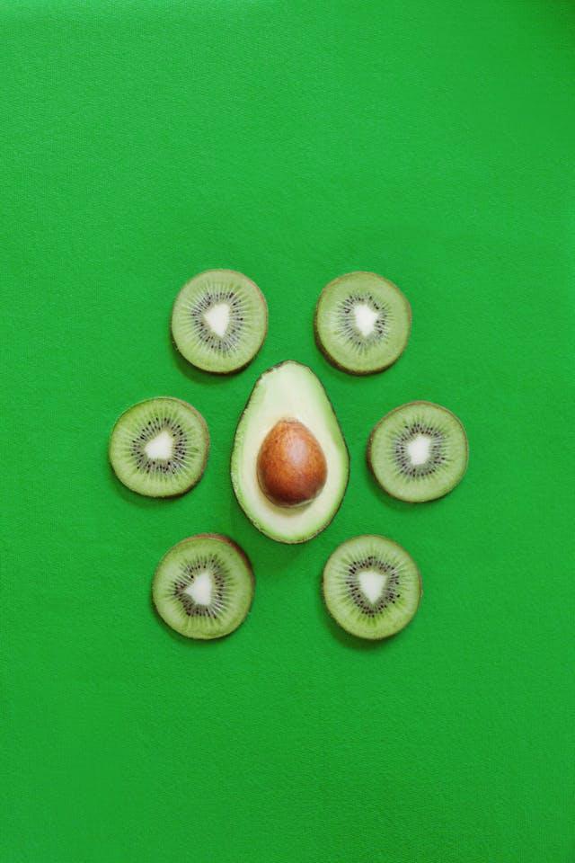 Moitié d'avocat entouré de rondelles de kiwis sur fond vert