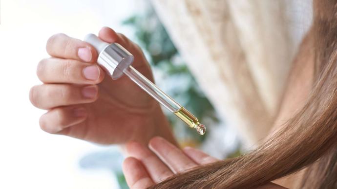 Main de femme qui tient une pipette d'huile au-dessus de ses cheveux longs châtains