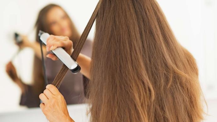 Femme de dos qui se lisse ses cheveux longs face à un miroir - visage flou