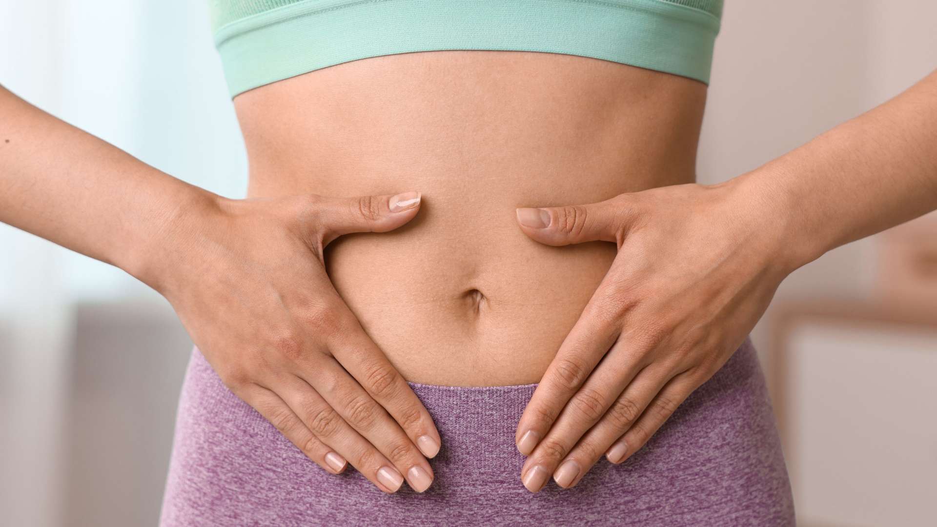 Ventre de femme avec haut vert et bas prune avec ses mains en coupe sur le ventre