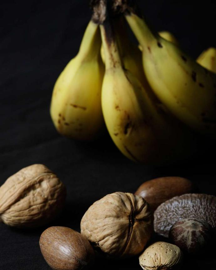 Trois bananes en arrière-plan avec noix et noix de macadamia au premier-plan ,sur fond noir