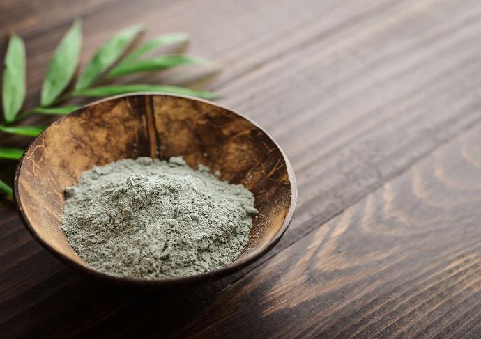 Argile verte en poudre dans bol en bois sur table en bois avec une feuille verte à côté