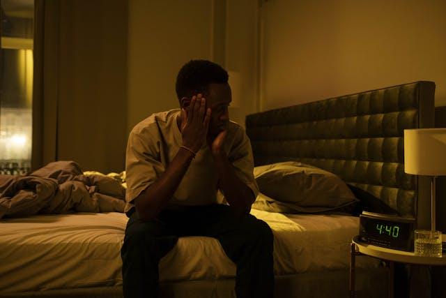 Homme assis dans son lit avec un réveil indiquant 4h40