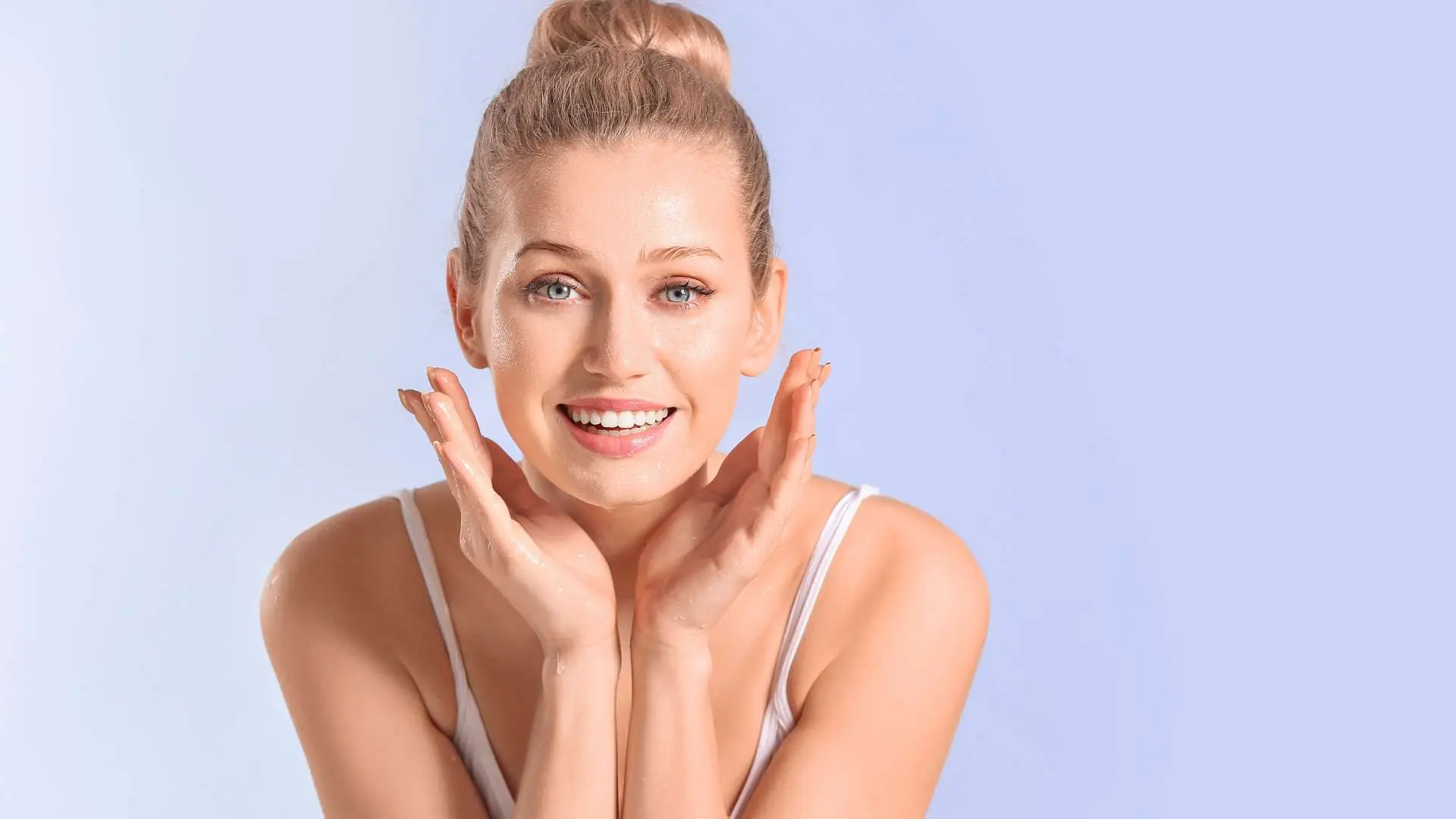 Femme blonde avec chignon qui sourit avec les mains en coupe autour de son visage sur fond parme