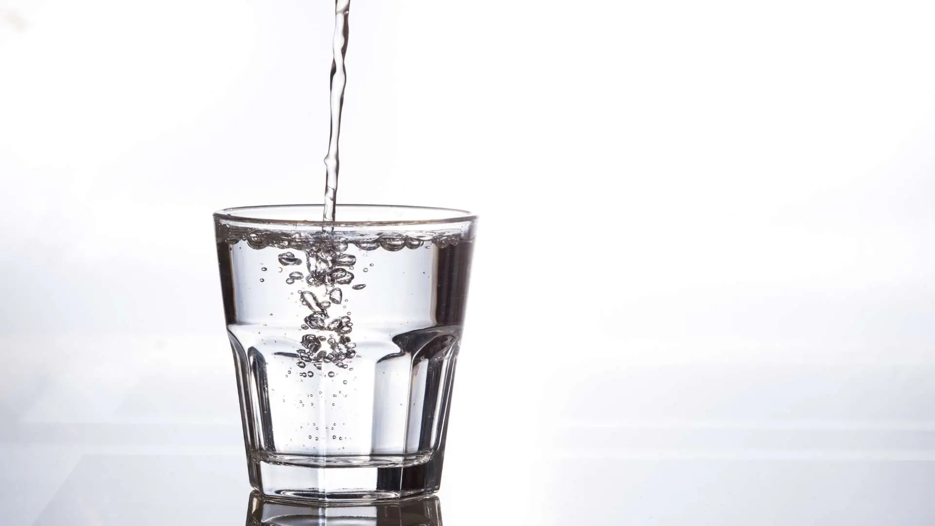 Verre d'eau avec filet d'eau qui coule dedans sur fond gris-blanc