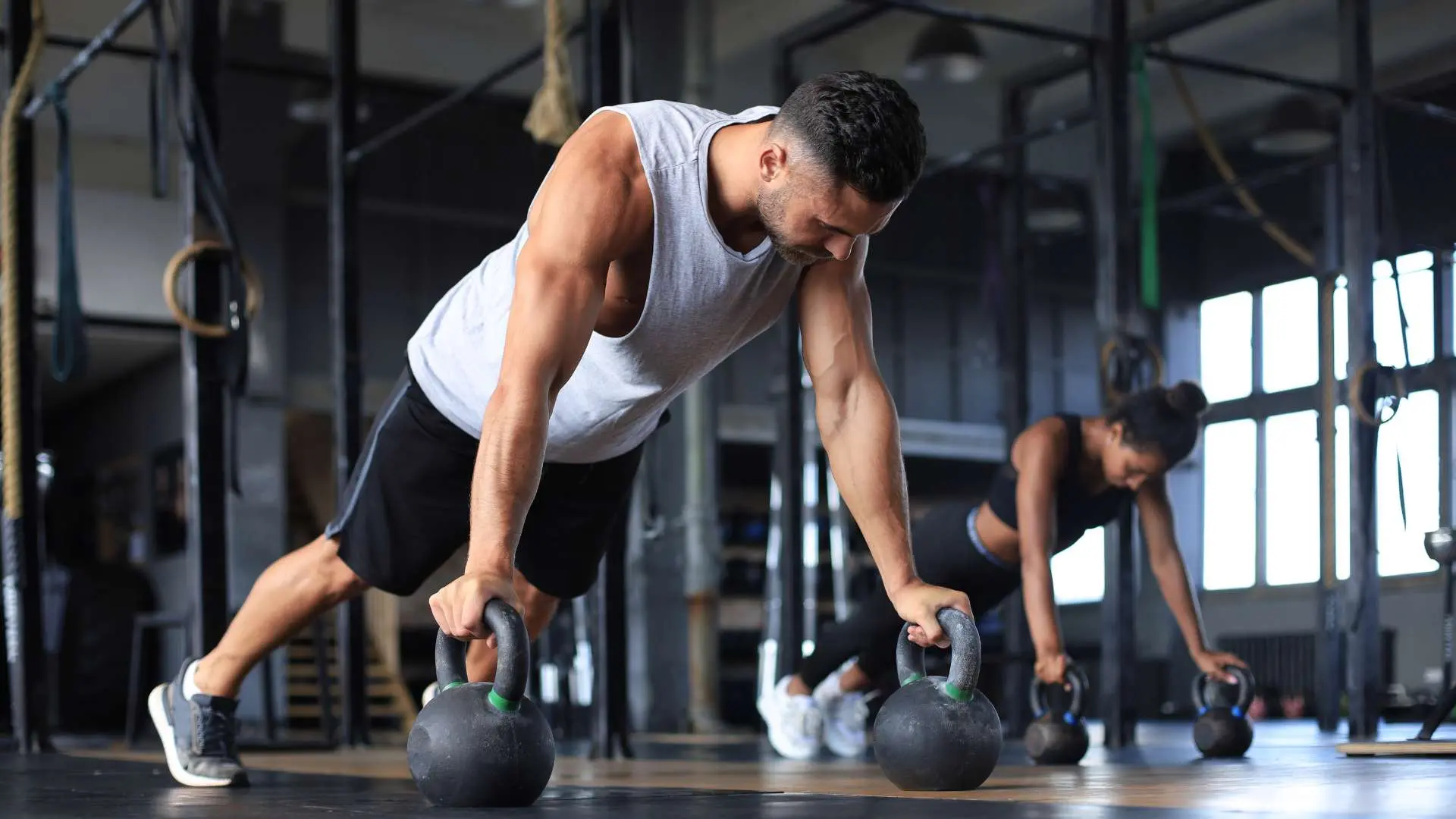 Un homme et une femme dans une salle de sport en position pompes sur des poids